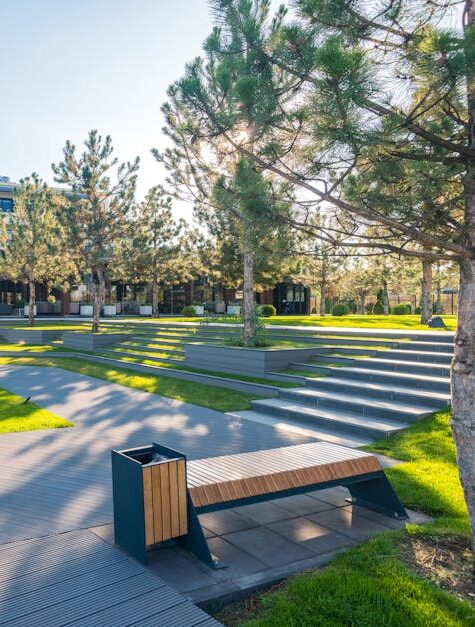 A modern urban park featuring an artistic statue, benches, and lush greenery under a bright sky.